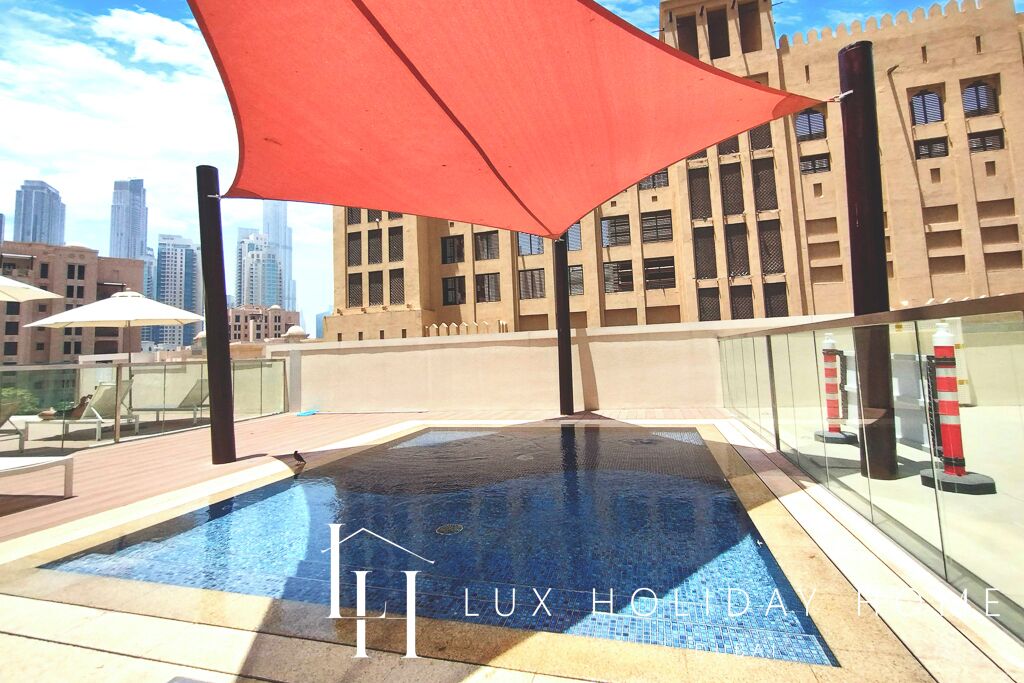 A rooftop pool area with a red umbrella, glass balustrade, and a cityscape view.