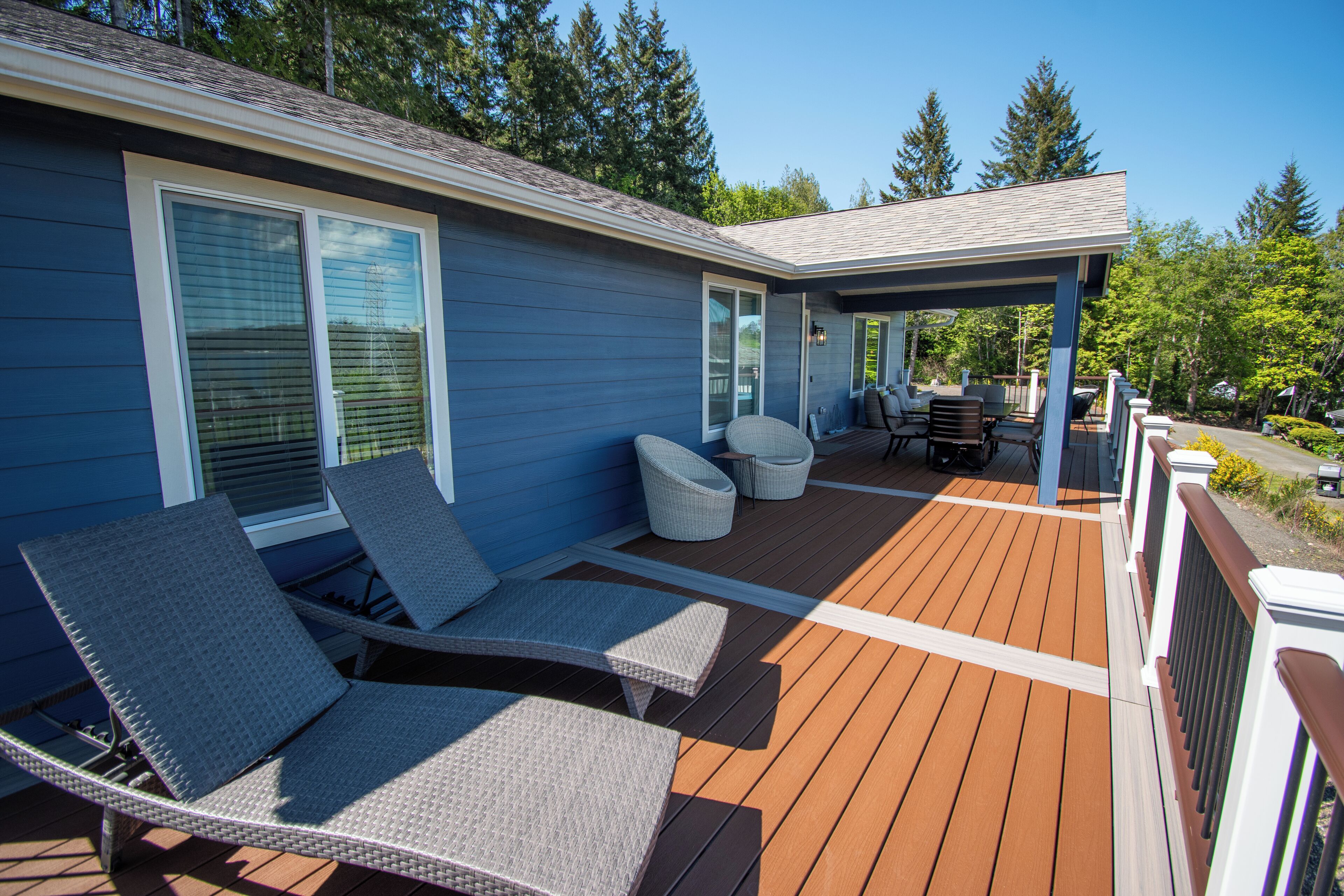 A covered deck with wicker lounge chairs, a small table, and a barbecue grill.