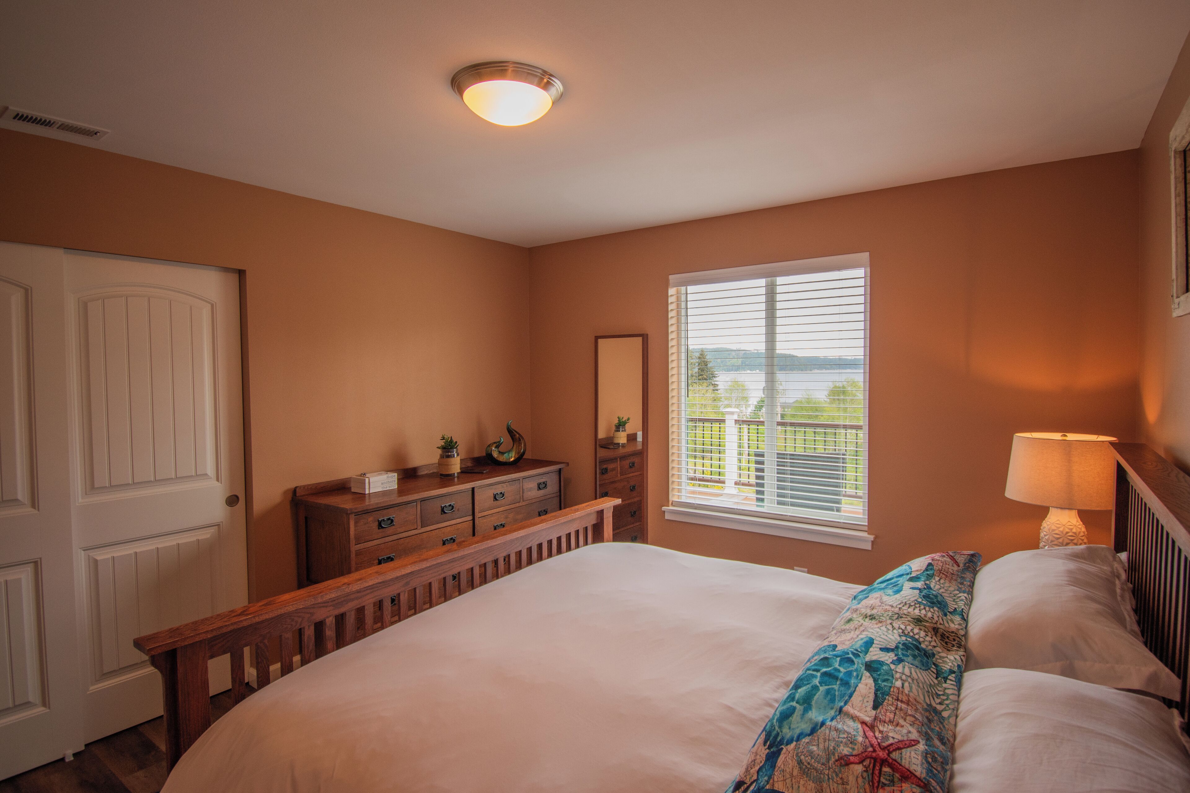 A bedroom with a large bed, a dresser, a nightstand, a window with blinds, and a ceiling light.