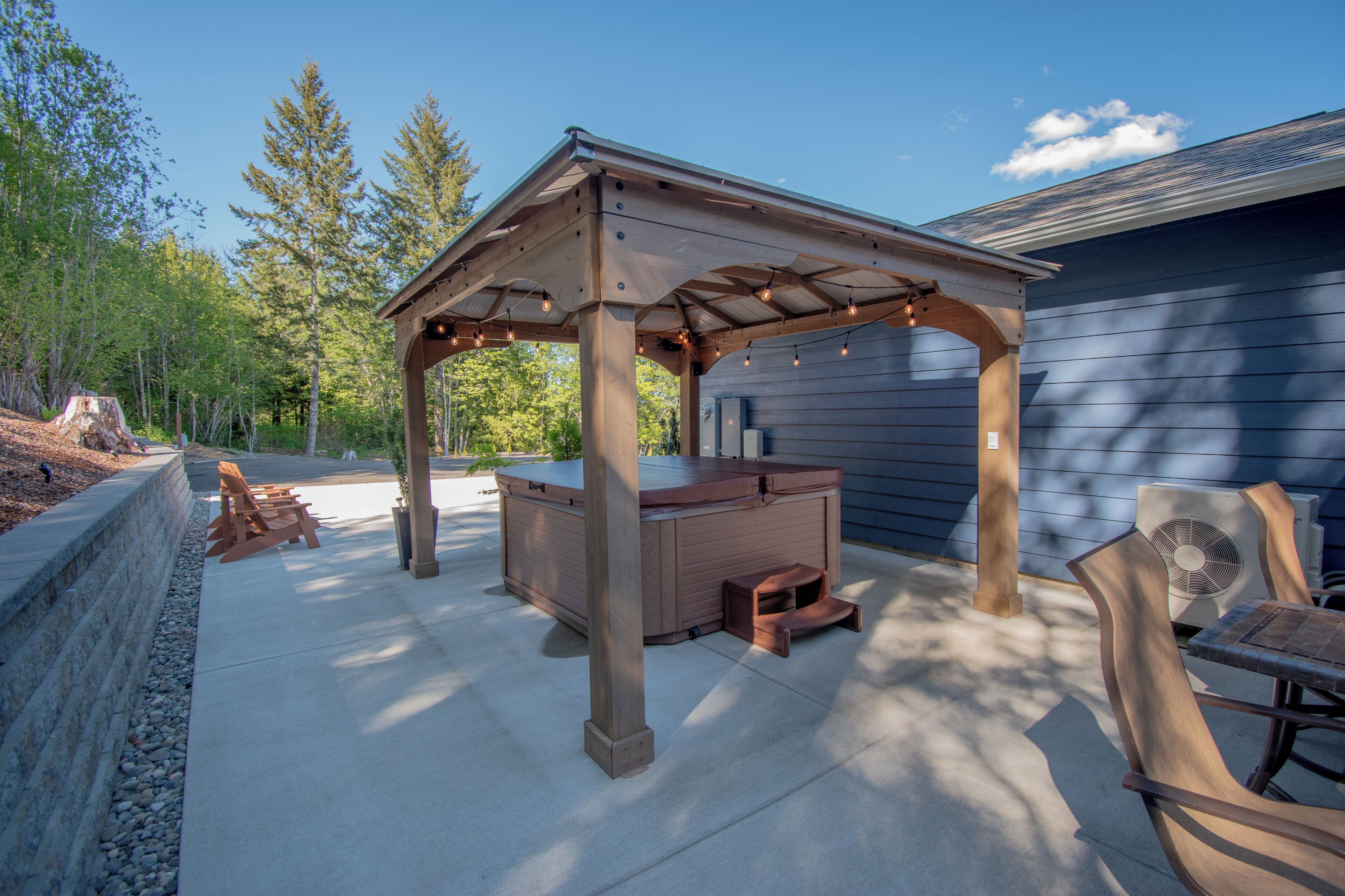 Un patio al aire libre con un jacuzzi, sillas de madera y una pérgola.