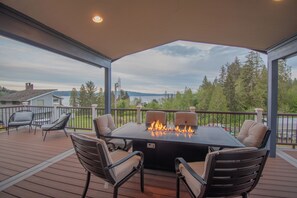 A covered outdoor deck with a fire pit table and four chairs. - Luxury Home Retreat-Sweeping Views + Large Hot Tub (Skokomish)