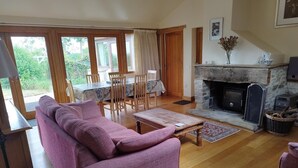 Una sala de estar acogedora con un sofá rosa, una mesa de centro de madera, una chimenea de piedra y un comedor con sillas y mesa de madera.