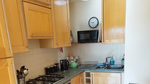 Una cocina con armarios de madera, estufa, horno, microondas, lavamanos y un reloj en la pared.