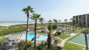Een resort met een zwembad, ligbedden, palmbomen en uitzicht op het strand.