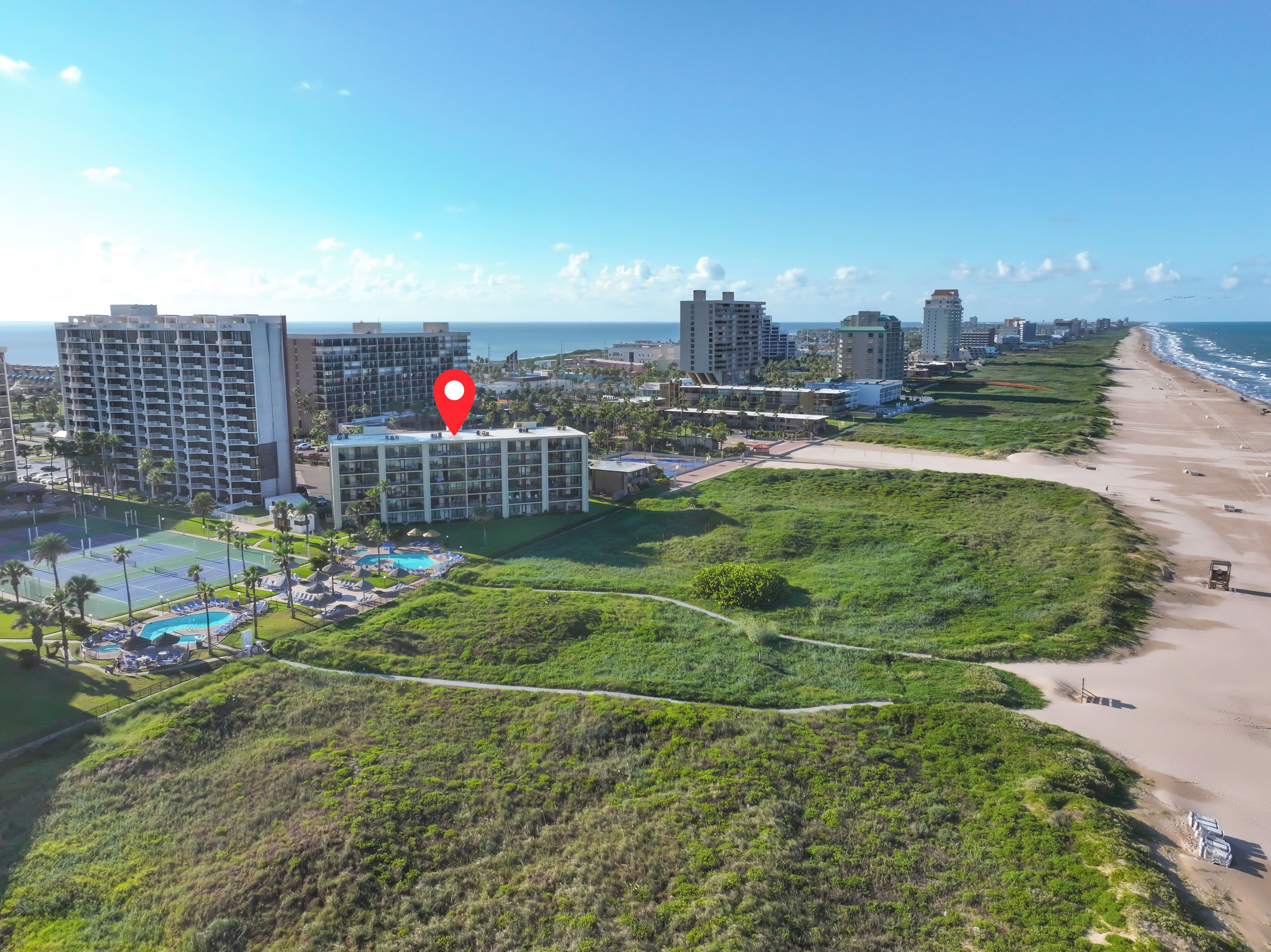 Un hotel costero con varios edificios altos, una playa y una zona de piscina.