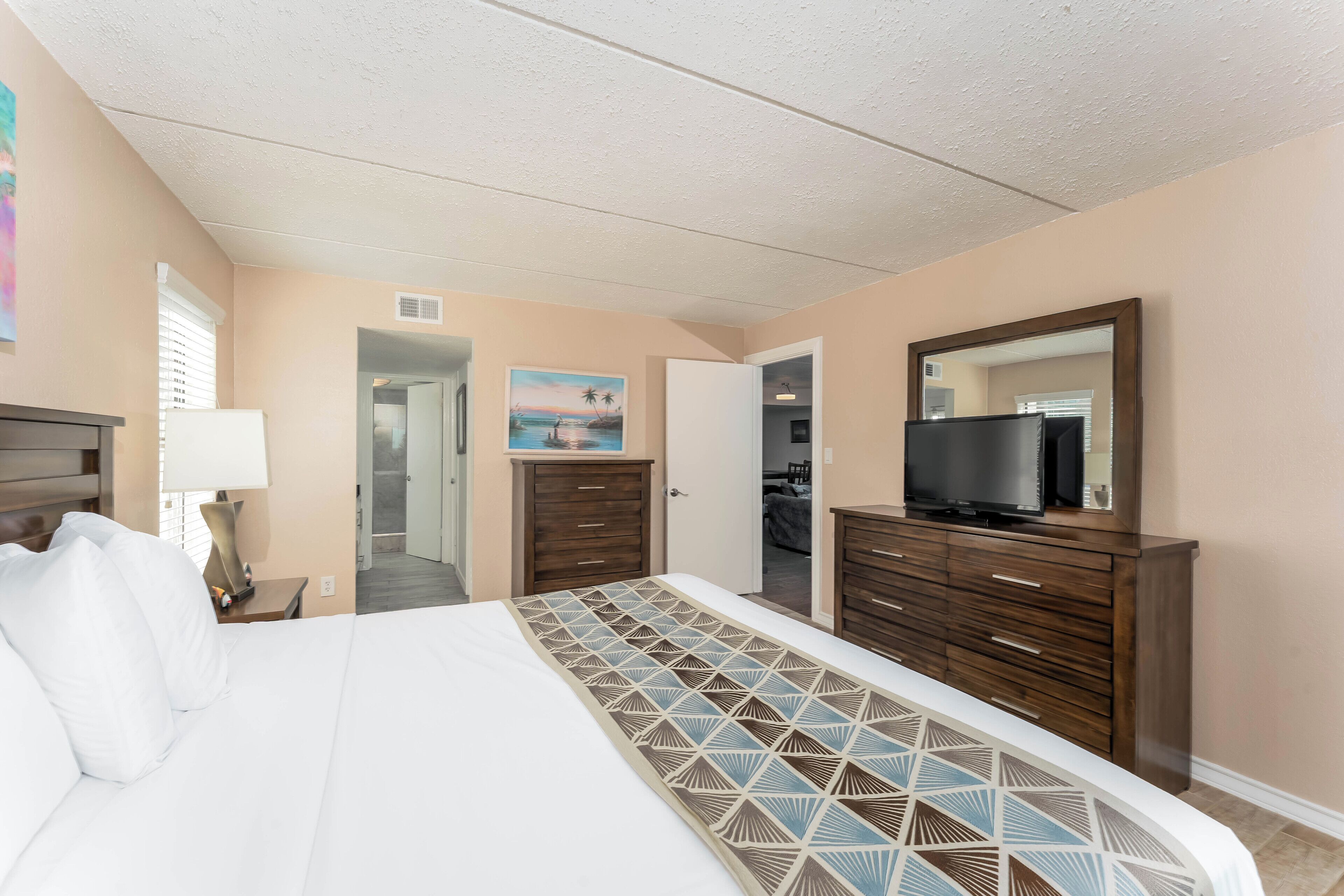 A hotel room with a large bed, a TV on a dresser, and a painting on the wall.