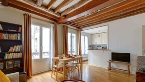 A spacious living room with a wooden ceiling, a dining area with a table and chairs, a bookshelf, a sofa, and a television on a stand. - Charming 1BR near Eiffel Tower & Les Invalides (Paris)