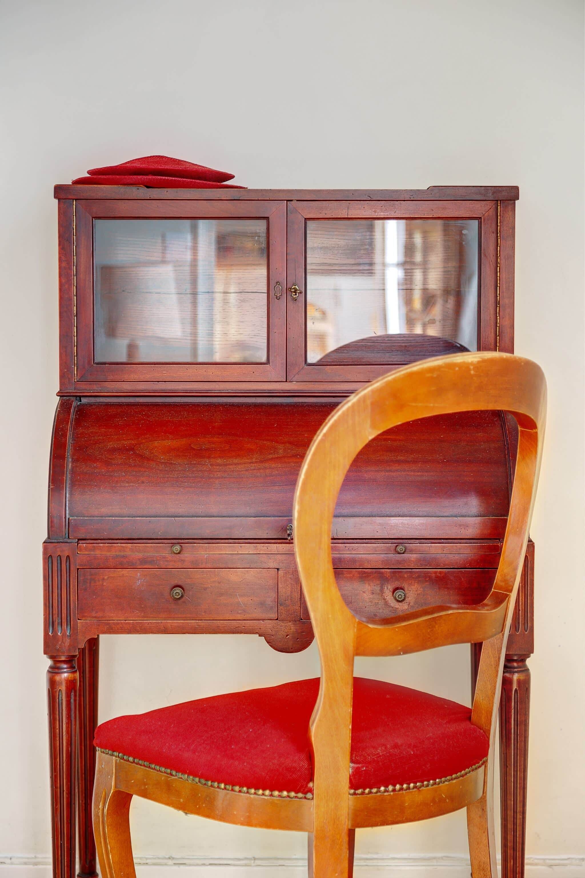 A wooden chair with a red cushion and a wooden cabinet with glass doors.