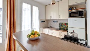 A kitchen with white cabinets, a microwave, a refrigerator, and a bowl of fruit on the counter. - Charming 1BR near Eiffel Tower & Les Invalides (Paris)