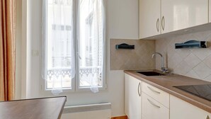 A kitchen with white cabinets, a sink, and a window with curtains. - Charming 1BR near Eiffel Tower & Les Invalides (Paris)