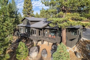 A cabin with a deck and a separate cabin attached, surrounded by trees and rocks.