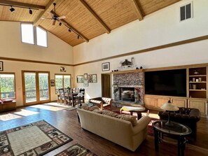 A spacious living room with a fireplace, a large TV, and a dining area with chairs and a table. - The Alpine Vista | Pets | Couples | Golf | Nakoma (Portola)