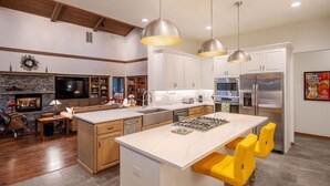 A modern kitchen with white cabinets, a central island with bar stools, stainless steel appliances, and pendant lighting. - The Alpine Vista | Pets | Couples | Golf | Nakoma (Portola)