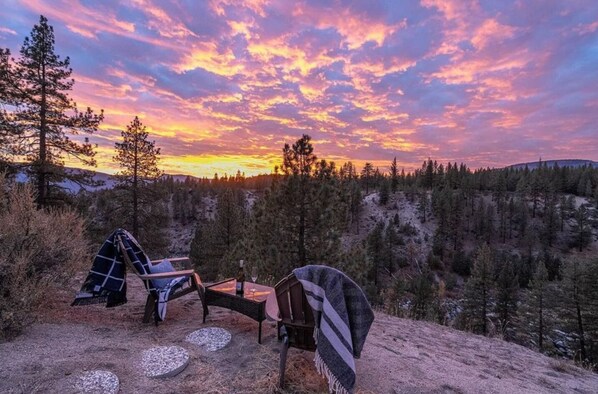 A campsite with two chairs and a table, surrounded by trees and a sunset view. - The Alpine Vista | Pets | Couples | Golf | Nakoma (Portola)