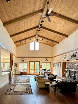 A spacious living room with a high ceiling, wooden beams, a fireplace, and a large window. - The Alpine Vista | Pets | Couples | Golf | Nakoma (Portola)