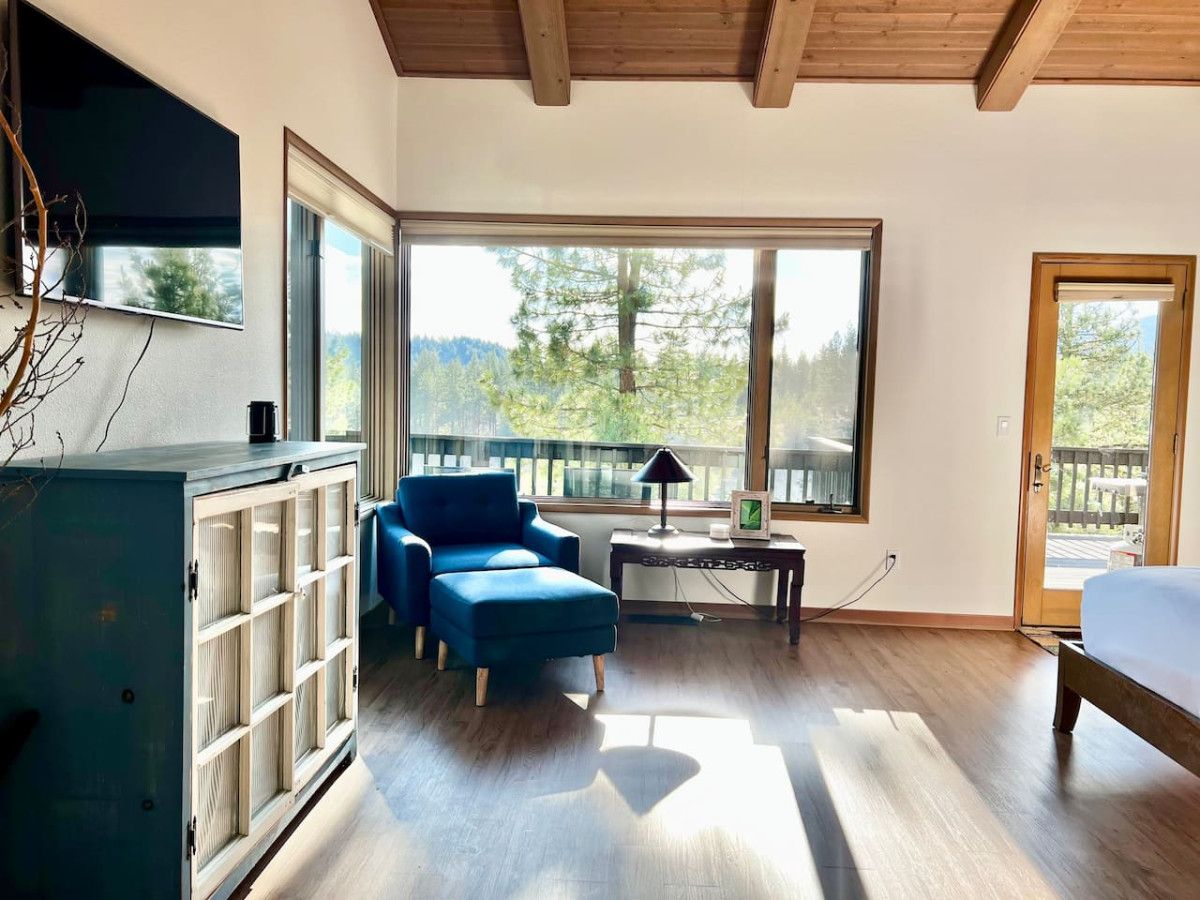 A room with a large window, a blue chair, a wooden cabinet, and a bed.