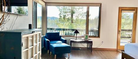 A room with a large window, a blue chair, a wooden cabinet, and a bed.