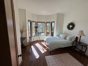 A bedroom with a bed, a tripod, a small table, a lamp, and a window with a view of trees.