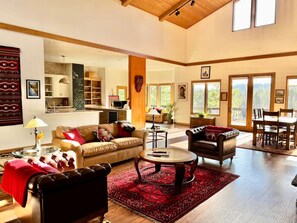A spacious living room with a high ceiling, a fireplace, and a dining area with a view of the outdoors.