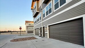 A multi-story residential building with a garage, a stop sign, and a clear sky. - Stylish Family Townhome with Relaxing Deck Views (Omaha)