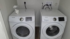Deux lave-linge Samsung à chargement frontal, de couleur blanche, se trouvent dans une buanderie dont le sol est en bois et dont le mur est blanc.