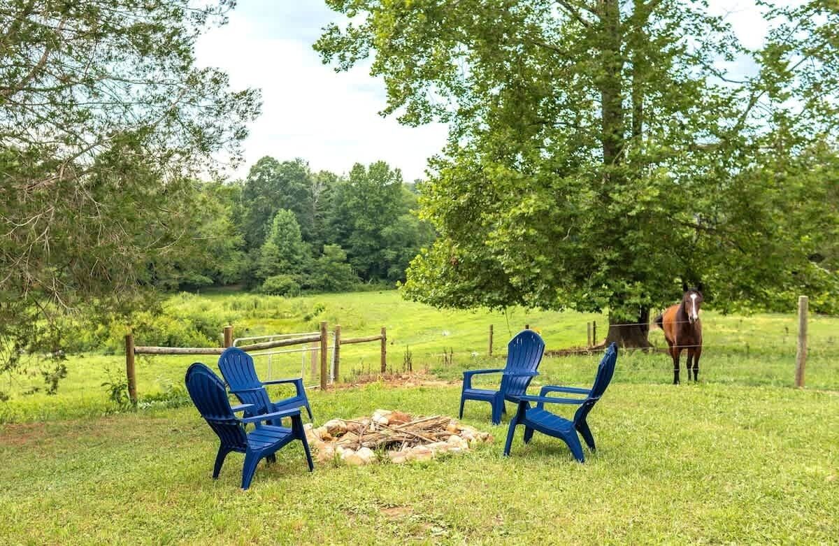 A grassy outdoor area with three blue chairs and a fire pit.