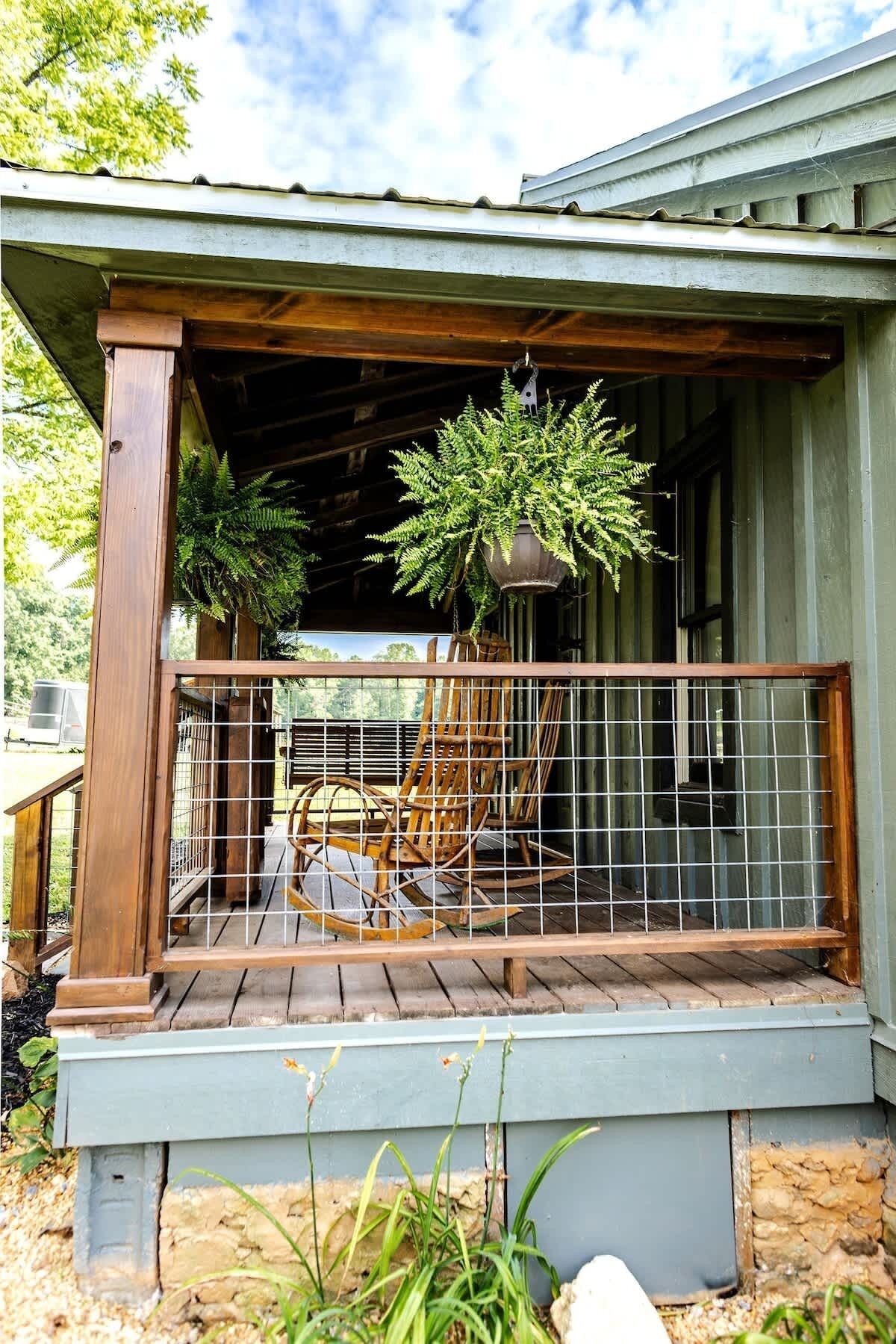 A wooden porch with a metal railing, a rocking chair, and hanging plants.