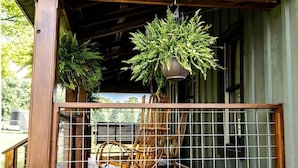 A wooden porch with a metal railing, a rocking chair, and hanging plants. - Equestrian Escape Sum (Blue Ridge)
