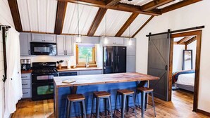 A modern kitchen with a central island, bar stools, a large refrigerator, and a sliding barn door. - Equestrian Escape Sum (Blue Ridge)
