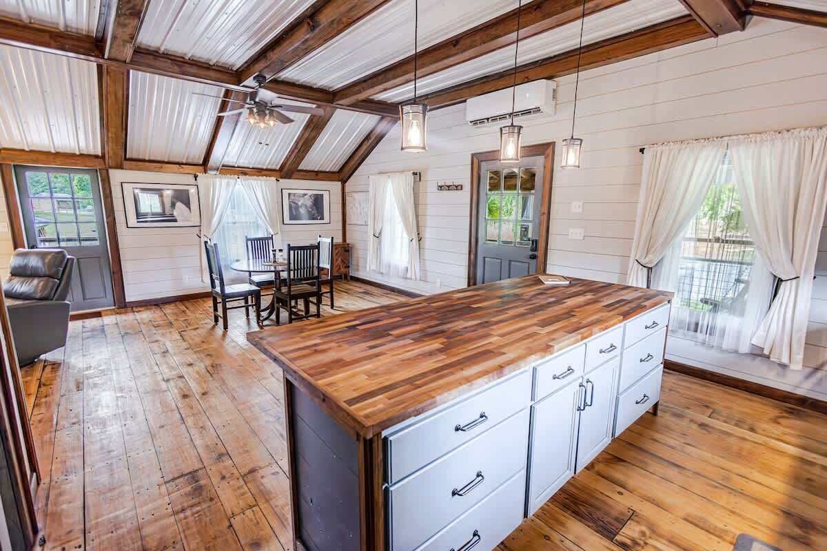 A spacious kitchen with wooden flooring, a central island with drawers, and a dining area with a table and chairs.