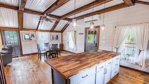 A spacious kitchen with wooden flooring, a central island with drawers, and a dining area with a table and chairs. - Equestrian Escape Sum (Blue Ridge)