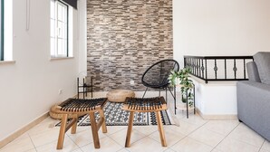 A modern living room with a patterned wall, a grey sofa, a black chair, and two wooden stools. - Oasis apartment - City center by HD (Faro)