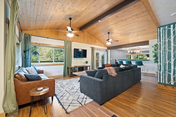 This airy living room features vaulted wood ceilings, large windows with scenic views, and plenty of cozy seating. Perfect for gathering, watching TV, or simply relaxing in a warm and inviting atmosphere.