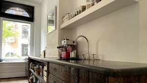 A kitchen with a wooden cabinet, a coffee machine, and a window with a view of buildings.