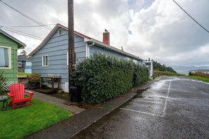 A residential house with a grey exterior, a red chair on the front lawn, and a hedge along the driveway.