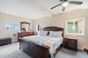 A bedroom with a large bed, a ceiling fan, a nightstand, a dresser, and a window with a view.