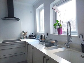 A modern kitchen with a white countertop, a stainless steel sink, a toaster, and a potted orchid by the window. - Free Parking/wifi, 3 Beds Sleep 6 Near Uni & Town! (Lancaster)