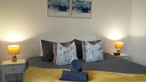 Une chambre à coucher comprenant un lit, deux lampes de chevet, une table de chevet et deux tableaux abstraits accrochés au mur.