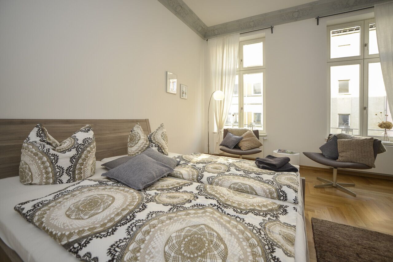 A bedroom with a large bed, a chair, and a window with curtains.