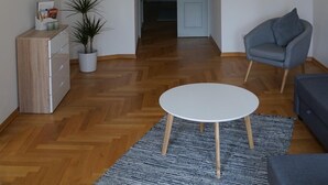 A modern living room with a wooden floor, a round white table, a grey armchair, a small potted plant, and a cabinet with magazines. - Konko Apartment near Zoo Leipzig (Leipzig)