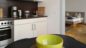 A modern kitchen with white cabinets, a stove, and a coffee maker. There is a dining table with a green bowl and two apples. - Konko Apartment near Zoo Leipzig (Leipzig)