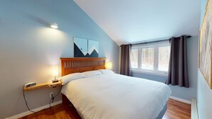 Een slaapkamer met een bed, nachtkastje, lamp en een raam met gordijnen.