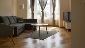 Een moderne woonkamer met een grijze bank, een ronde salontafel en een televisie op een witte kast.