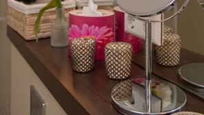 Een wastafel met een ronde spiegel, een vaas met bloemen en decoratieve objecten.