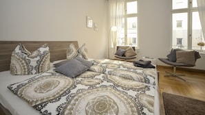 Een slaapkamer met een groot bed, een stoel en een raam met gordijnen.