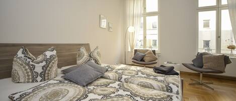 A bedroom with a large bed, a chair, and a window with curtains.