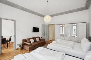 Une chambre moderne avec un canapé marron, un lit avec du linge de lit blanc, une télévision et une armoire aux portes miroir.