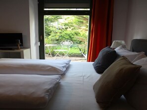 Een hotelkamer met een bed, kussens, een televisie en uitzicht op groen.