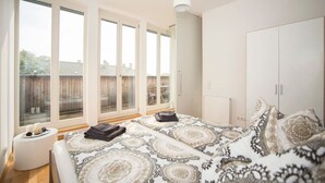 Une chambre avec deux lits, de grandes fenêtres, une armoire et une table de chevet avec des bougies.