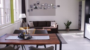 Ein modernes Wohnzimmer mit einer Couch, einem Esstisch mit Stühlen, einem Couchtisch, einer Lampe und einer Wand mit gerahmten Bildern.